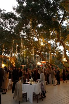 a group of people standing around a table with food and drinks on it under some trees