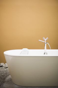 a white bath tub sitting on top of a cement floor next to a yellow wall