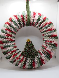 a crocheted christmas wreath with a green and red tree hanging from the front