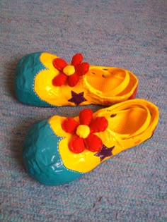 a pair of yellow and blue shoes with flowers on them sitting on the floor next to a carpet