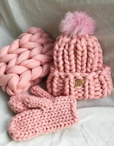 three pink knitted hats and mittens laying on top of each other, one with a pom - pom