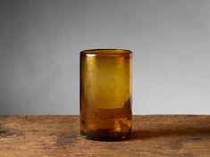 a brown glass sitting on top of a wooden table next to a gray wall in the background