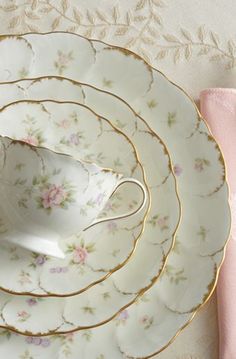 a stack of white and gold plates with pink napkins next to it on a table