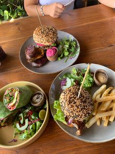 two plates with burgers and fries on them sitting on a table next to a woman