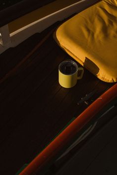 a yellow cup sitting on top of a wooden floor next to a blanket and knife