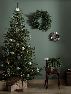 a christmas tree in front of a wall decorated with wreaths and ornaments, next to a chair