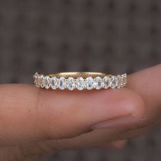 a woman's hand holding a gold ring with white stones on it and the band is