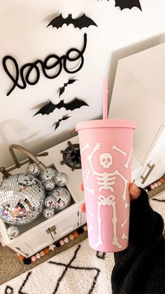 a person holding up a pink cup with a skeleton on it and bats flying around