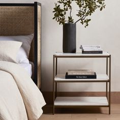 a bed with white sheets and pillows next to a black vase filled with green plants