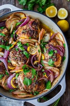 a pan filled with meat and onions on top of a table next to lemons