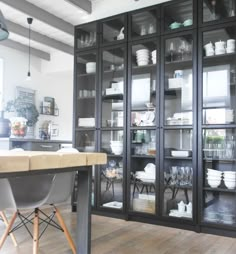 an open glass cabinet in a kitchen with wooden flooring and white dishes on the shelves