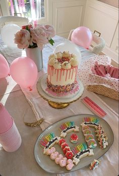 a birthday cake and cookies on a table with balloons, streamers and other decorations