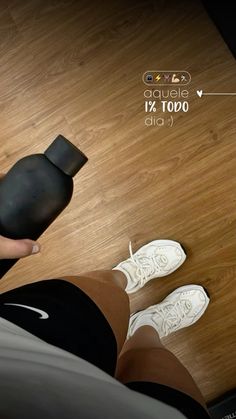 a person standing on a wooden floor next to a black object and white shoes,