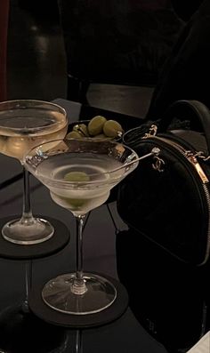 two martini glasses sitting on top of a table next to a black bag and purse