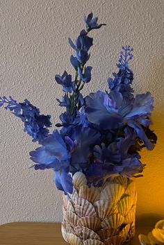 a vase with blue flowers on a table next to a yellow light and a wall