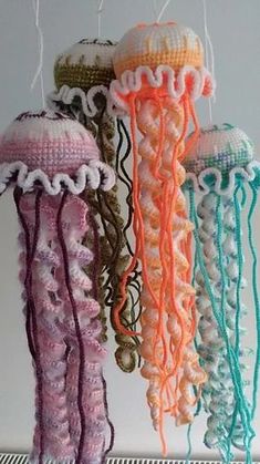 three crocheted jellyfishs hanging from strings on a shelf in a room