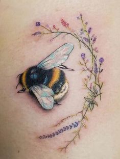 a small tattoo on the side of a woman's stomach with a bee and flowers