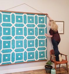 a woman standing next to a blue and white wall hanging on the side of a wooden frame