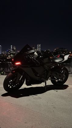 a black motorcycle parked in front of a city at night with the lights on it