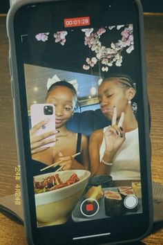 two women sitting at a table looking at their cell phones with food on the screen