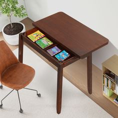 a wooden table with books on it and a chair next to it in front of a potted plant