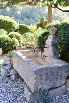 a stone sink in the middle of some rocks and gravel with a potted plant next to it