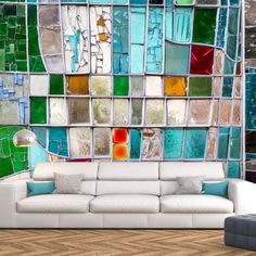 a white couch sitting in front of a window covered in colorful glass tiles on the wall