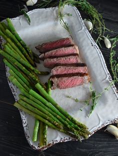 steak, asparagus and garlic on a white plate with some green garnish