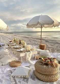 an outdoor table set up on the beach for a picnic with white linens and umbrellas