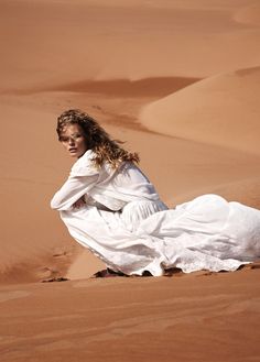 a woman sitting in the desert wearing a white dress