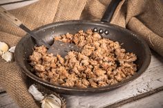 a skillet filled with meat and garlic on top of a wooden table next to a sack