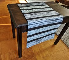 a wooden table topped with a black and white striped table runner on top of a hard wood floor