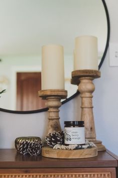 two candles are sitting on top of a dresser with pine cones and other items in front of the mirror