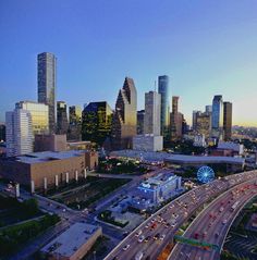 an aerial view of the city skyline at dusk with cars driving on the road and tall buildings in the background