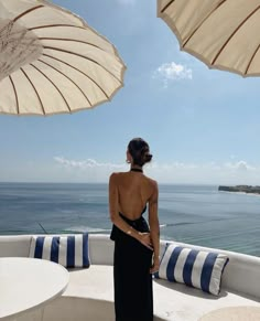 a woman standing on top of a boat looking out at the ocean with two umbrellas