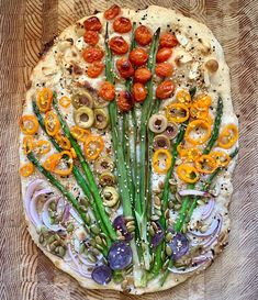 a pizza topped with lots of veggies on top of a wooden table covered in toppings