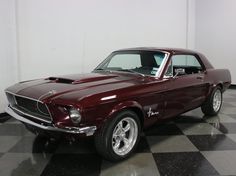 a red mustang sitting on top of a black and white checkerboard floor next to a wall