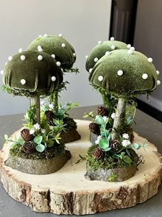 two green trees with white balls on them sitting on a tree stump in the middle of a table