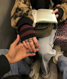 two hands holding an open book while sitting on the floor with other people around them