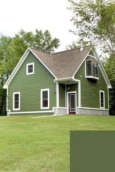 a green house with white trim on the front and side windows, sitting in a grassy yard