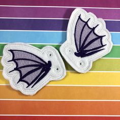 two embroidered butterfly patches sitting on top of a rainbow striped table cloth covered surface with white stitching