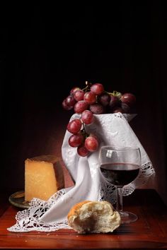 a glass of wine and some grapes on a table next to a piece of bread