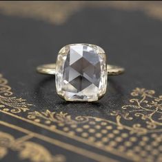 an old - fashioned ring with a cushion cut diamond sits on top of a book