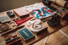 the table is covered with various items such as books, pens, scissors and t - shirts