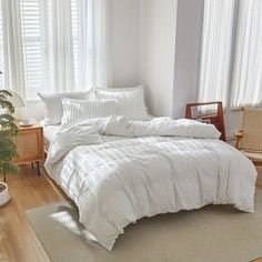 a bed with white comforter and pillows in a bedroom next to a plant on the floor