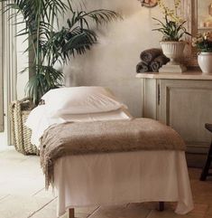 a bed with white sheets and pillows in a room next to potted palm trees