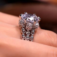 a woman's hand holding a ring with an oval shaped diamond surrounded by smaller diamonds