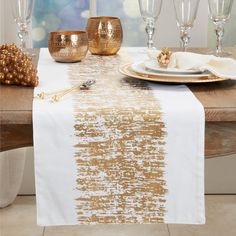 a white and gold table runner on top of a wooden table with wine glasses next to it