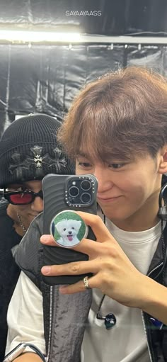 a boy taking a selfie with his cell phone in front of him and another person behind him