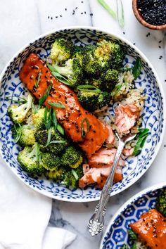 two bowls filled with salmon and broccoli on top of a white tablecloth